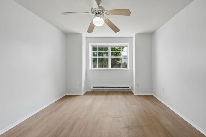Bright and airy room with modern ceiling fan, stylish wood flooring, and large window offering natural light.