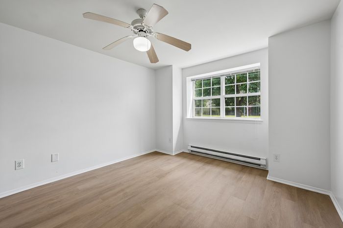 Bright and airy room featuring elegant wooden flooring, a stylish ceiling fan, and a large window with a scenic tree view.