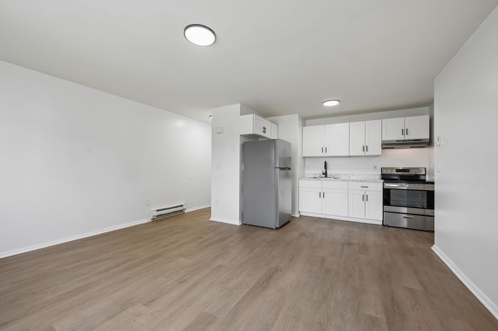 Modern open-plan kitchen with sleek white cabinets, stainless steel appliances, and elegant flooring, ideal for contemporary living.