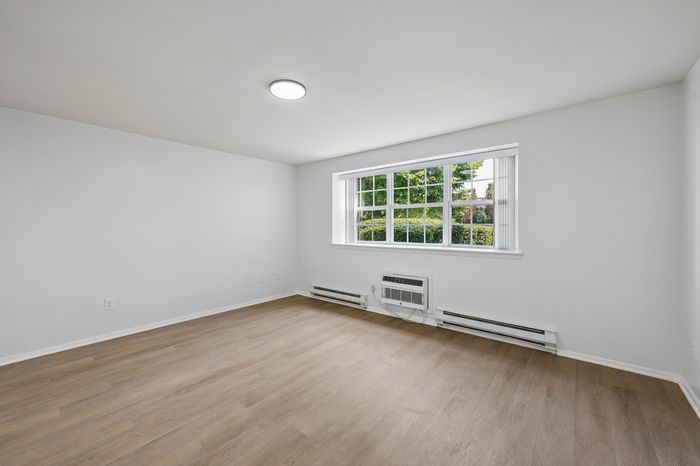 Bright and inviting room with large window and modern light fixture, showcasing new hardwood floors, perfect for a cozy retreat or creative studio.