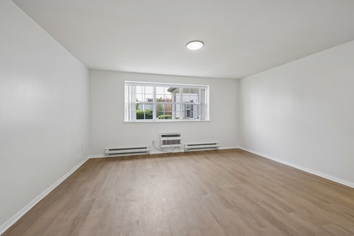 Bright and inviting empty room with large window, elegant wood flooring, and ample natural light perfect for customization.