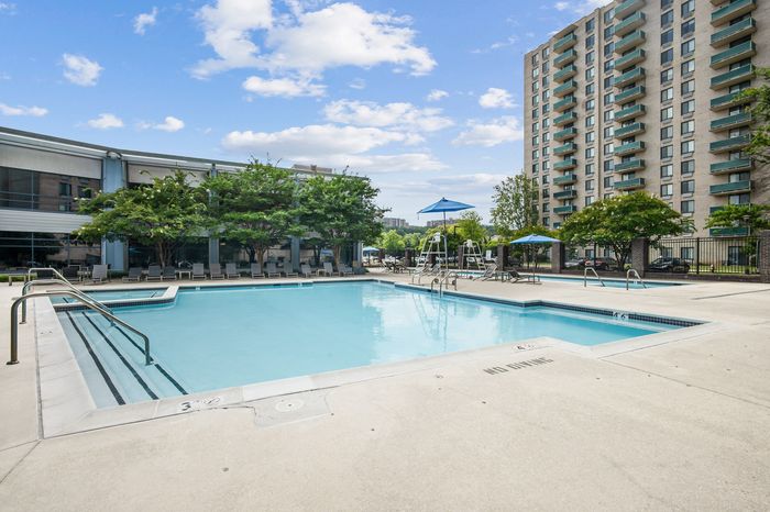 Luxurious apartment complex with a sparkling outdoor swimming pool, surrounded by lush greenery and modern high-rise buildings, perfect for relaxation and leisure.