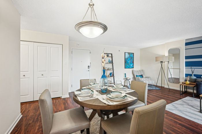 Chic open-plan dining area with elegant decor, showcasing a round table set for four, against a stylish blue accent wall and modern wooden flooring.