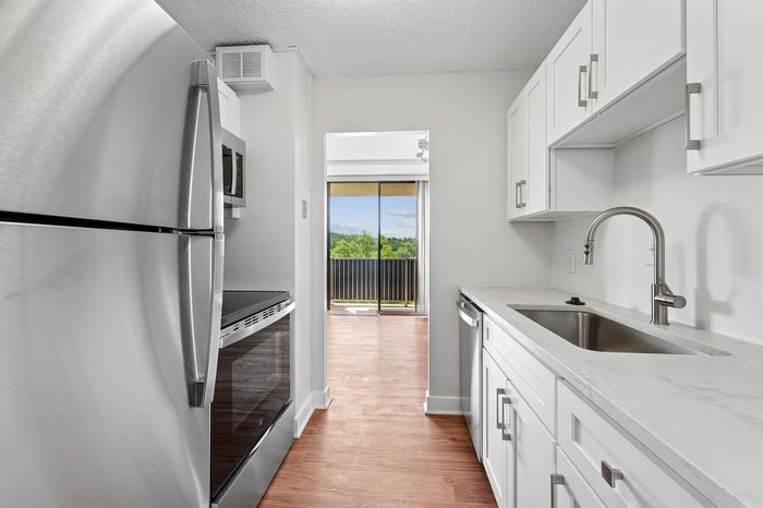 Modern kitchen with sleek stainless steel appliances, bright white cabinetry, and a picturesque view through the balcony doors.