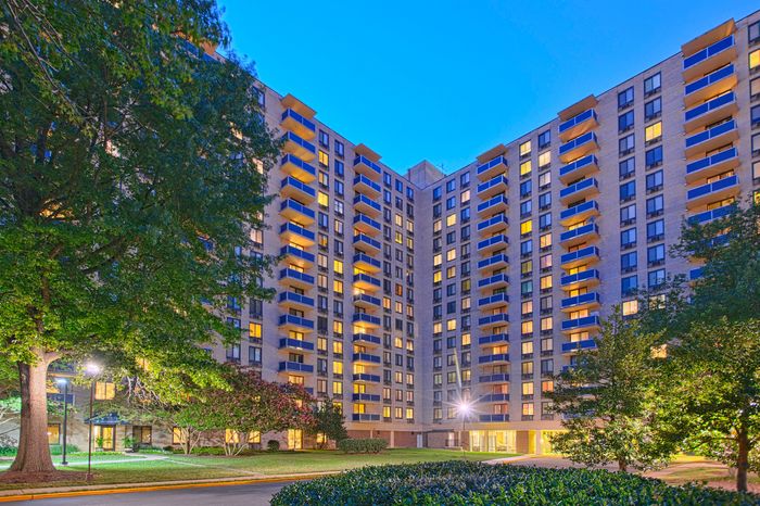 Elegant high-rise apartment building illuminated at dusk, surrounded by lush greenery and tranquil pathways.