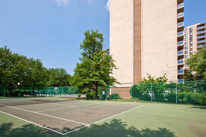 Modern apartment building with adjacent tennis courts surrounded by lush greenery under a clear blue sky.