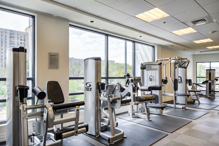 Bright and modern apartment fitness center equipped with state-of-the-art exercise machines and floor-to-ceiling windows offering scenic views.