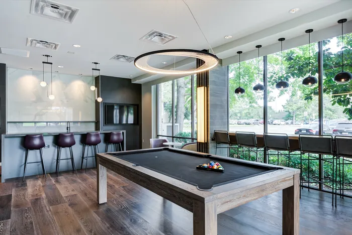 Elegant lounge area with a sleek pool table, contemporary bar seating, and panoramic windows offering lush garden views.