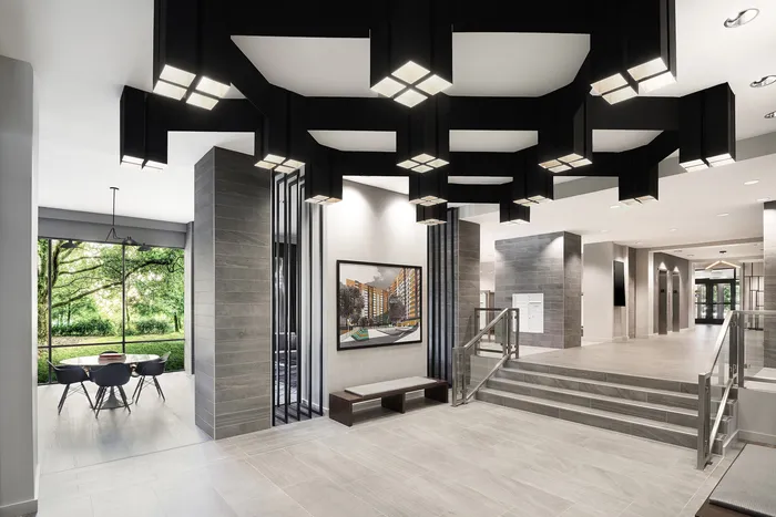 Elegant, modern apartment lobby with a striking geometric ceiling, large windows offering lush garden views, and a sophisticated gray interior.