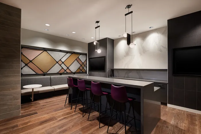 Modern lounge area featuring a sleek bar with purple chairs, cozy seating, and stylish pendant lighting.