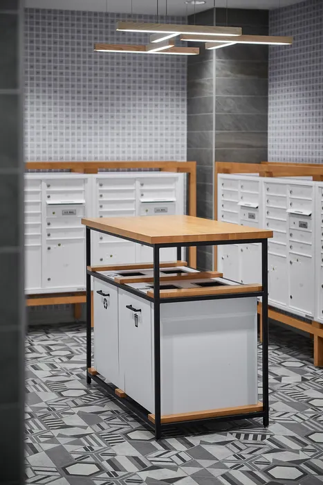 Modern mailroom with stylish geometric flooring, sleek mailboxes, and a chic central recycling station with overhead contemporary lighting.
