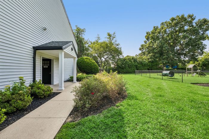 Charming apartment exterior featuring a welcoming entrance, lush landscaping, and an expansive green lawn ideal for outdoor activities.