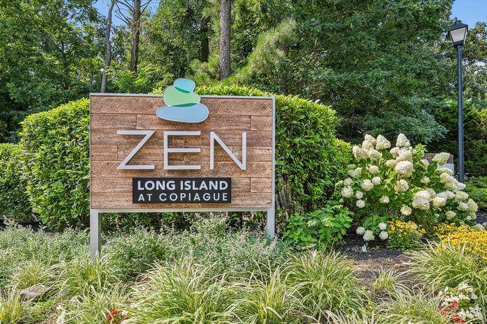 Inviting Zen Long Island entrance sign surrounded by lush greenery and vibrant flowers.