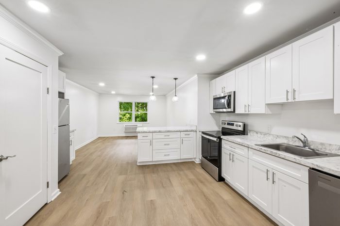 Bright, contemporary kitchen and living area with sleek white cabinetry, stainless steel appliances, and elegant wood flooring.