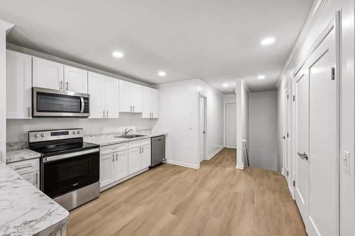 Modern kitchen with sleek white cabinets, stainless steel appliances, and elegant marble countertops, accented by warm hardwood floors.