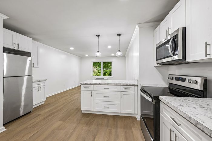 Modern kitchen with sleek stainless steel appliances, elegant white cabinetry, and stylish marble countertops, featuring warm wood flooring and abundant natural light.