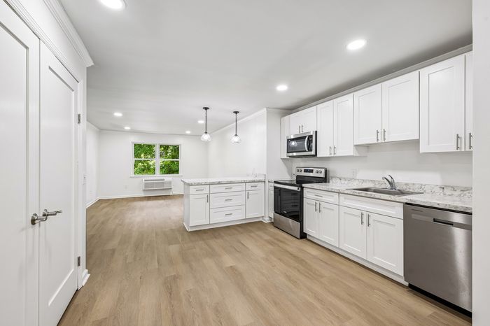 Bright and modern open-plan kitchen and living area with sleek white cabinetry, stainless steel appliances, and elegant wooden flooring.