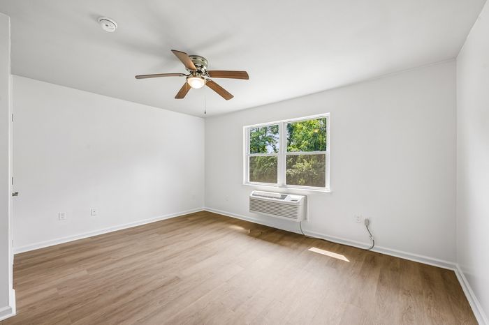 Bright, airy room with sleek hardwood floors, a stylish ceiling fan, and large window inviting natural light.