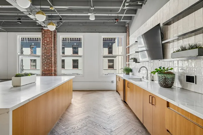 Elegant urban kitchen with sleek countertops, modern appliances, and large windows highlighting exposed brick accents.