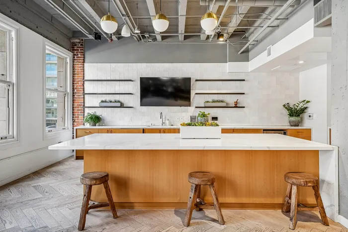 Modern kitchen with sleek wooden cabinets, white countertops, and stylish open shelving, accentuated by exposed brick and industrial ceiling features.