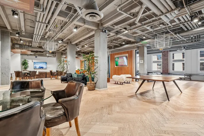Modern communal space with sleek industrial design, featuring stylish seating, herringbone wood floors, and ample natural light.