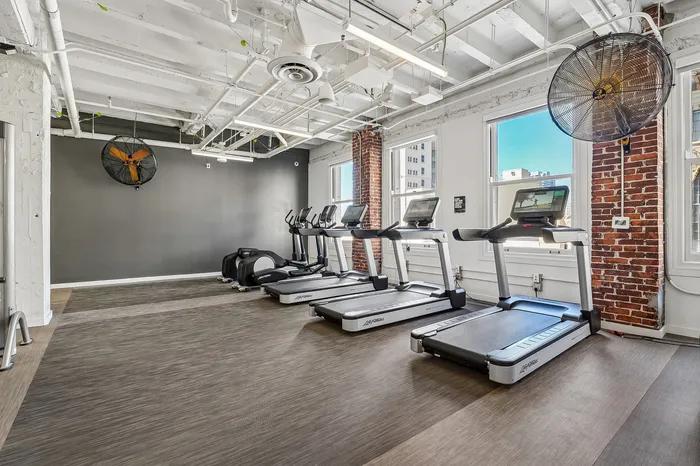 Contemporary fitness center with state-of-the-art treadmills, exposed brick accents, and ample natural light.