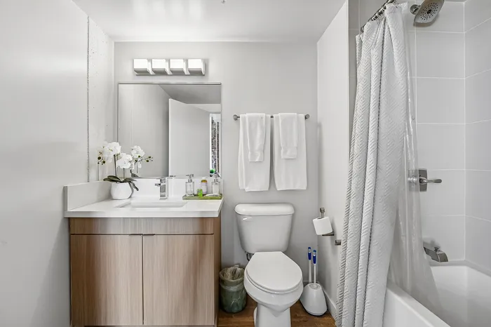 Modern bathroom featuring elegant white and wood vanity, sleek lighting, and a luxurious shower setup.