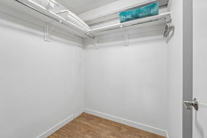 Spacious walk-in closet with hardwood flooring and ample shelving, perfect for organized living.