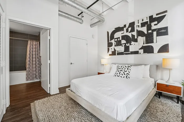 Chic bedroom showcasing modern decor with abstract wall art, sleek furniture, and an inviting en-suite bathroom.