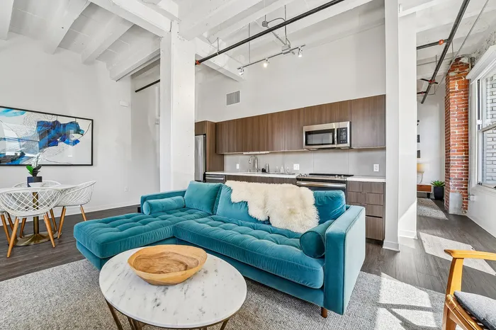 Contemporary apartment interior featuring a chic teal sofa, stylish wood kitchen cabinets, and a cozy modern dining area with artistic decor.