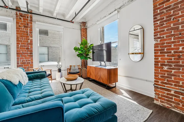 Chic urban living room with exposed brick walls, a plush teal sofa, and ample natural light.