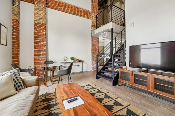 Chic industrial-style loft with exposed brick, modern staircase, cozy seating, and a sleek entertainment center.
