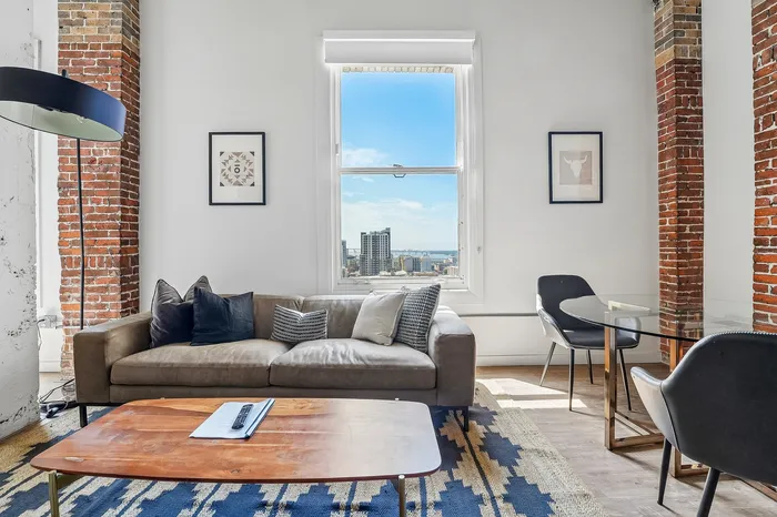 Chic urban living room with exposed brick accents, a comfortable sofa, modern artwork, and a stunning cityscape view through a large window.