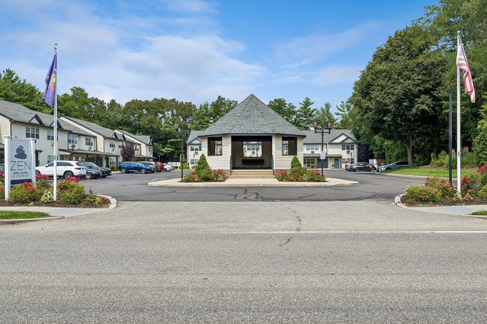 Charming apartment complex in Oyster Bay featuring well-maintained gardens, ample parking, and a welcoming pavilion under a clear blue sky.