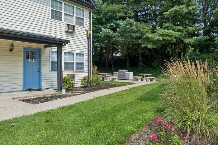 Charming apartment exterior with a welcoming blue door, surrounded by lush greenery and a scenic picnic area.