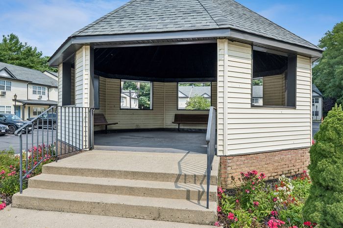 Charming gazebo with inviting benches, nestled in a vibrant garden setting, perfect for relaxation in a tranquil neighborhood.