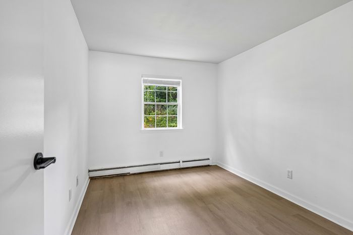 Bright and inviting room with freshly painted white walls and sleek hardwood floors, illuminated by natural light from a charming window.