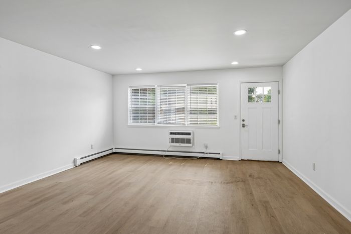 Bright and inviting living space with sleek hardwood flooring, modern recessed lighting, and large windows offering ample natural light.