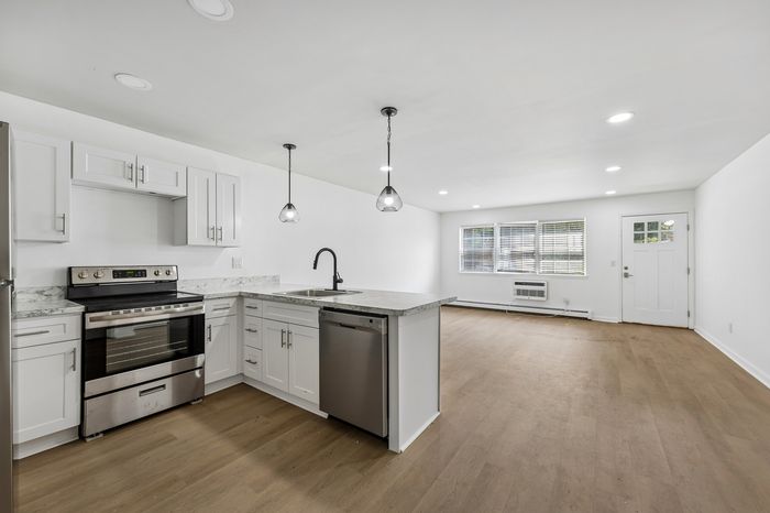Contemporary open-plan kitchen and living area featuring elegant wood flooring, stylish pendant lights, and modern stainless steel appliances.