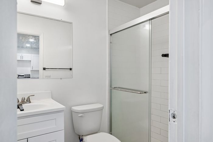 Sleek and modern bathroom with elegant glass shower, pristine white vanity, and a large mirror reflecting natural light.
