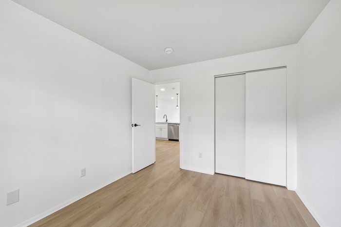 Bright, airy bedroom with sleek hardwood floors and a glimpse into a modern kitchen, perfect for contemporary living.