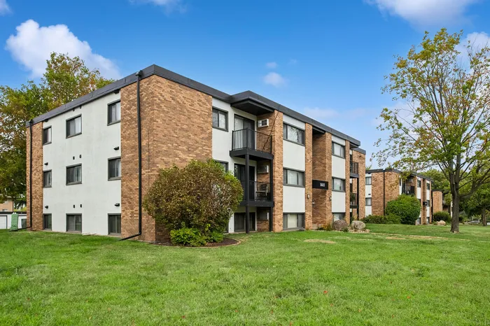 Charming brick apartment complex with lush green lawns and a vibrant blue sky backdrop.