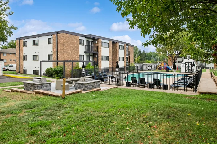 Charming apartment complex with a large outdoor pool, modern barbecue area, and lush green surroundings, perfect for relaxation and leisure.