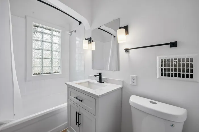 Elegant and modern bathroom featuring a sleek vanity with marble countertop, stylish lighting, and a classic white bathtub with a privacy window.