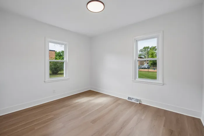 Bright and airy room with elegant hardwood flooring, featuring two large windows offering lush green views.