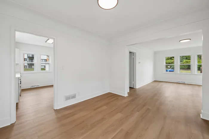 Bright and spacious open-concept living and dining area with elegant hardwood floors and large windows overlooking greenery.