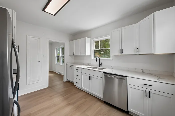 Contemporary kitchen with sleek white cabinetry, stainless steel appliances, and elegant wood flooring.