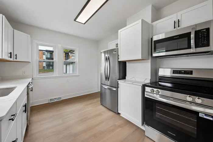 Modern kitchen with sleek stainless steel appliances, bright white cabinets, and large windows offering natural light.