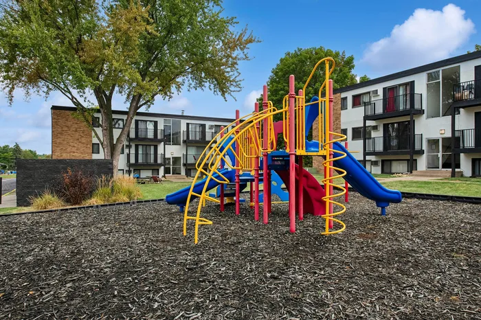 Charming apartment complex with modern balconies, featuring a vibrant playground surrounded by lush greenery.