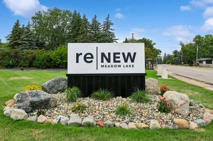 Charming reNew Meadow Lake entrance sign set amidst a beautifully landscaped area with vibrant greenery and colorful flowers.